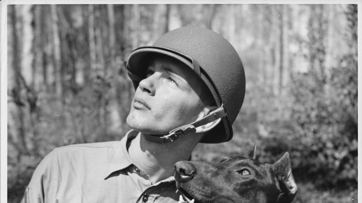 “Pfc. Homer J. Finley, Jr. USMC, is shown with his canine leatherneck buddy, ‘Jan’ spotting a make-believe sniper in a tree during the day’s rugged training period. Pvt. ‘Jan’, a Doberman Pinscher, was enlisted by his owner for the duration.”