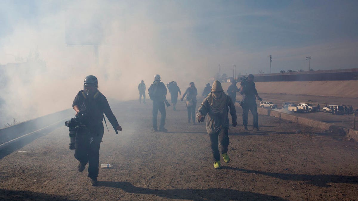 Migrants run from tear gas launched by U.S. agents, amid photojournalists covering the Mexico-U.S. border, after a group of migrants got past Mexican police at the Chaparral crossing in Tijuana, Mexico, Sunday, Nov. 25, 2018. The mayor of Tijuana has declared a humanitarian crisis in his border city and says that he has asked the United Nations for aid to deal with the approximately 5,000 Central American migrants who have arrived in the city. (AP Photo/Rodrigo Abd)