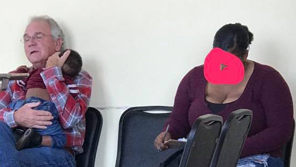 Joe Hale holds Jade West's son Jayce as she fills out paperwork at the doctor's office. A post on social media about the two strangers went viral commenting on the "hope" this moment gave.