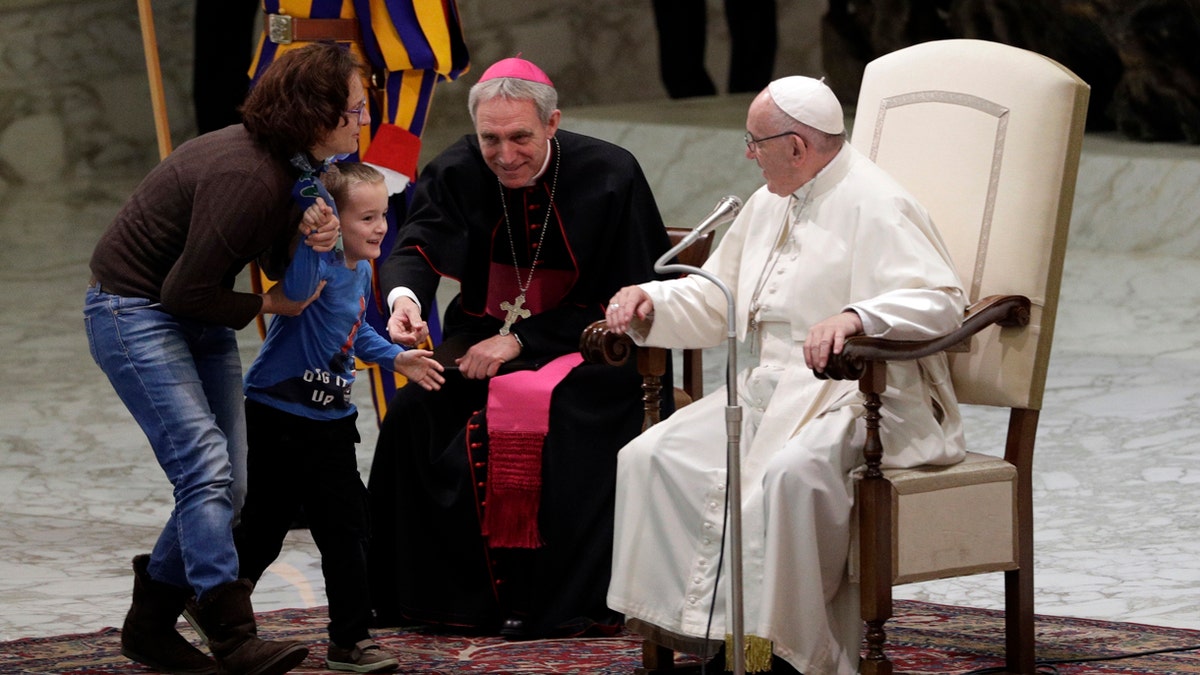 A child is taken away after getting up to the area where Pope Francis is sitting, right, during his weekly general audience in the Paul VI Hall at the Vatican.