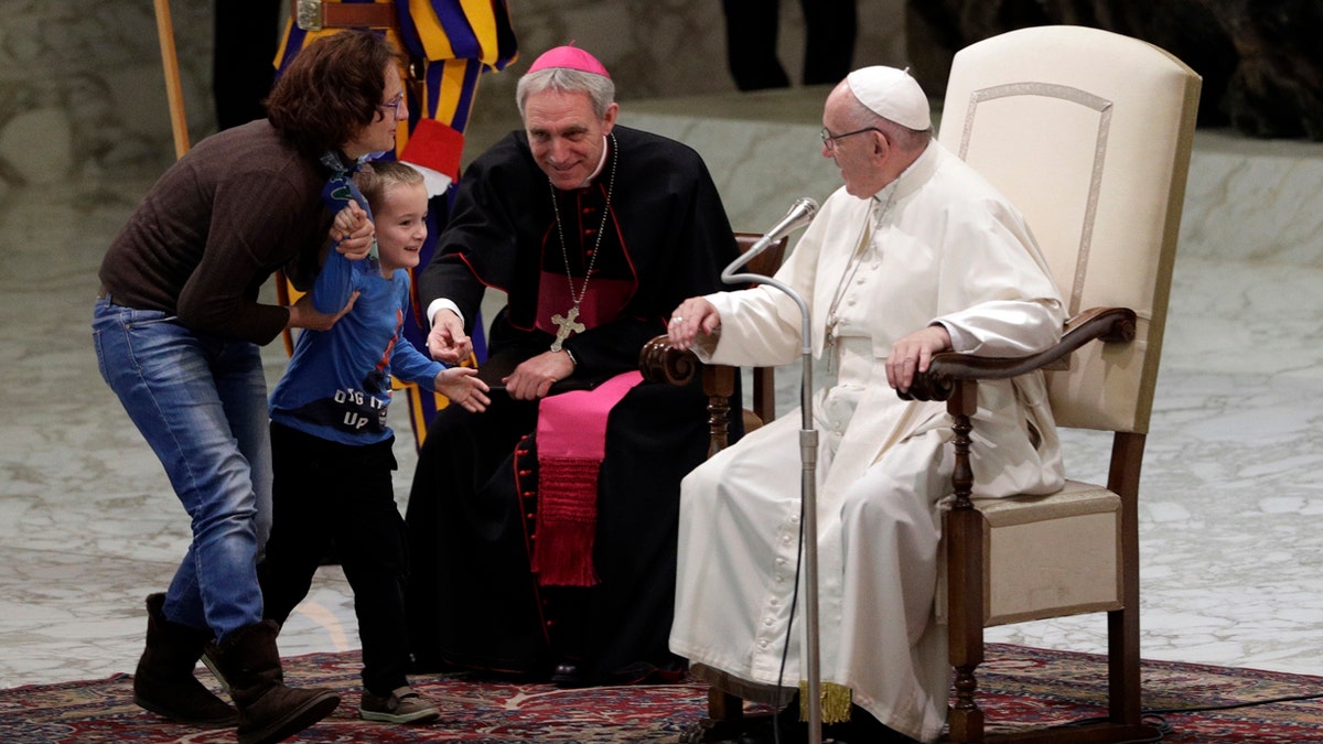 A child is taken away after getting up to the area where Pope Francis is sitting, right, during his weekly general audience in the Paul VI Hall at the Vatican.
