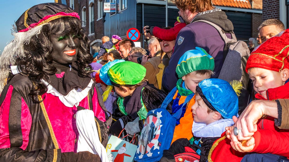 A Black Pete interacts with children during the arrival of Sinterklaas in Monnickendam, Netherlands, Saturday, Nov. 17, 2018. White people often daub their faces with black paint when they dress up to play the character. Opponents say such depictions of Black Pete promote racist stereotypes. Supporters defend the sidekick of Sinterklaas, the white-bearded, red-robed Dutch version of St. Nicholas, as a traditional children's character. (AP Photo/Patrick Post)