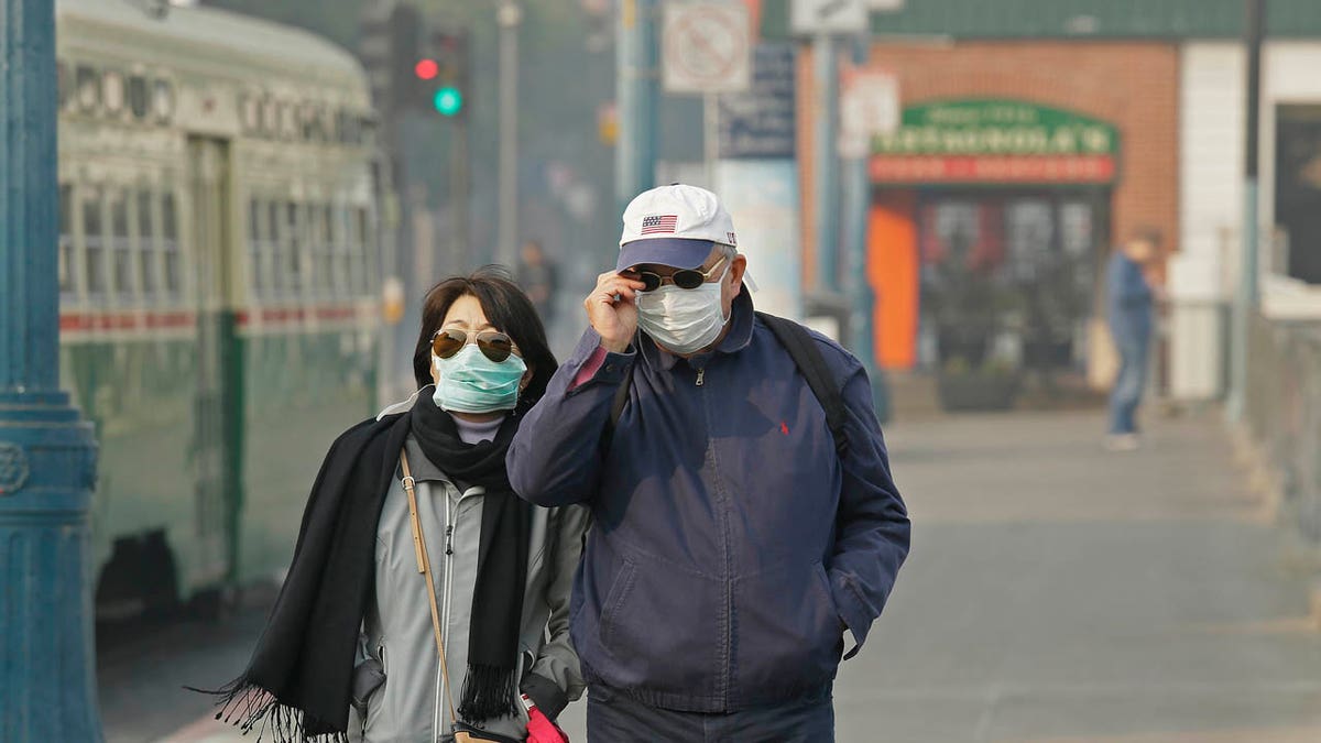 A couple wears masks while walking at Fisherman's Wharf through smoke and haze from wildfires Friday, Nov. 16, 2018, in San Francisco.