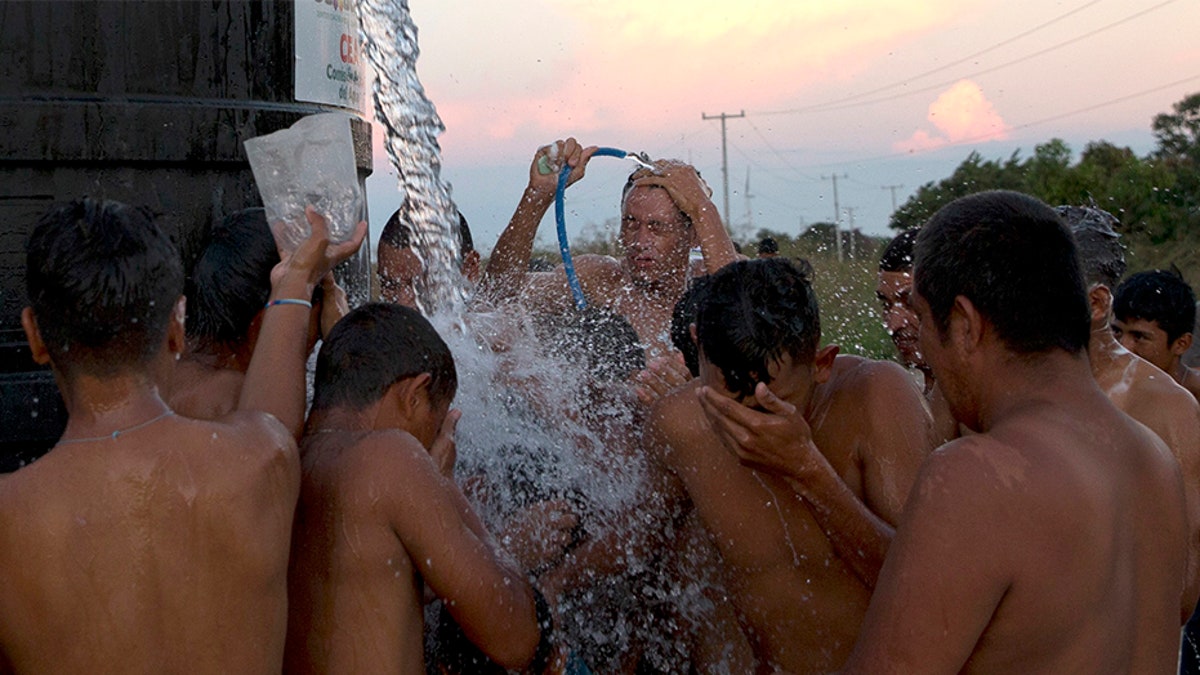 A man filling a water tank on a truck pauses to spray migrants with water to help them shower in Juchitan.