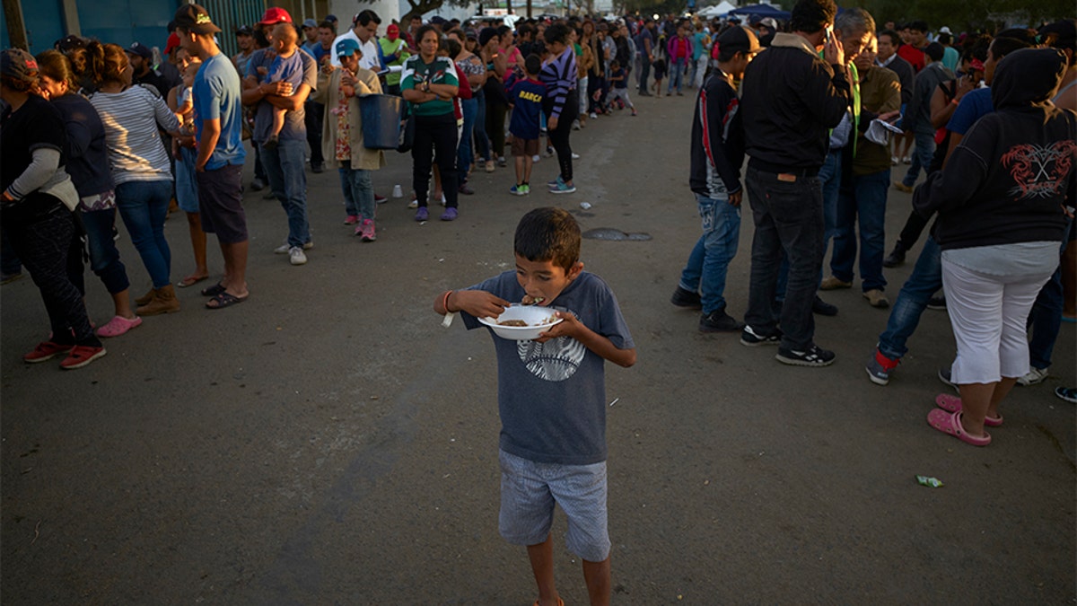 A boy eats as others wait in line for dinner outside of a shelter housing members of the migrant caravan in Tijuana.