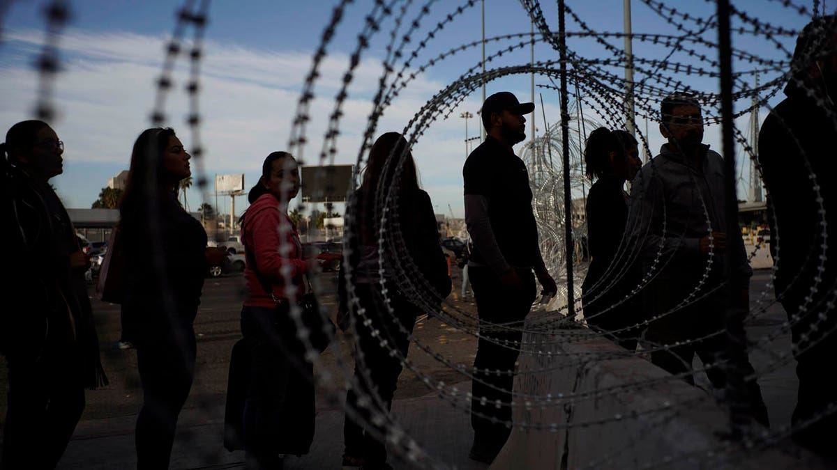 Pedestrians stand near barbed wire at a legal Mexico-U.S. border crossing as they prepare to leave Tijuana, Mexico, Monday, Nov. 19, 2018.