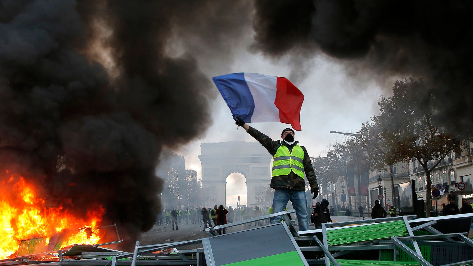 A demonstrator waves the French flag onto a burning barricade on the Champs-Elysees avenue with the Arc de Triomphe in the background, during a demonstration against the rise of the fuel taxes in Paris, Nov. 24, 2018.
