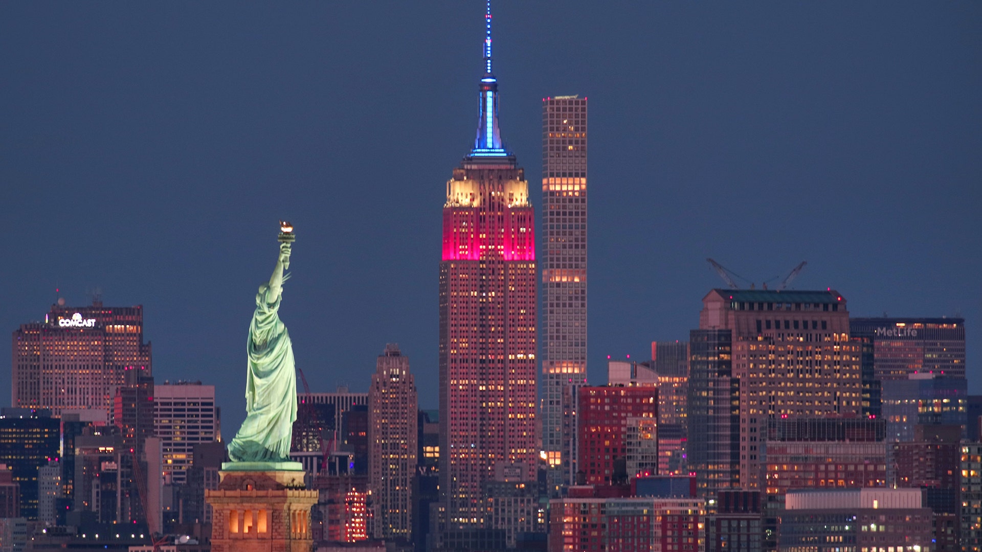 The Empire State Building is lit in red, white, and blue next to the Statue of Liberty in honor of Veterans Day as seen from Bayonne, New Jersey, November 11, 2018. 