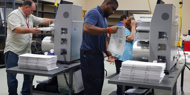 Election workers place ballots into electronic counting machines, Sunday, Nov. 11, 2018, at the Broward Supervisor of Elections office in Lauderhill, Fla. The Florida recount began Sunday morning in Broward County. (Joe Cavaretta /South Florida Sun-Sentinel via AP)