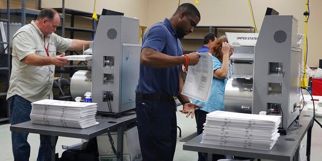 Election workers place ballots into electronic counting machines, Sunday, Nov. 11, 2018, at the Broward Supervisor of Elections office in Lauderhill, Fla. The Florida recount began Sunday morning in Broward County. (Joe Cavaretta /South Florida Sun-Sentinel via AP)