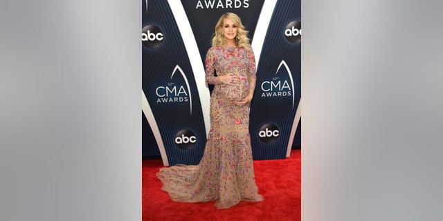 Carrie Underwood cradles her baby bump as she steps out in a floor-length floral gown at the CMAs.