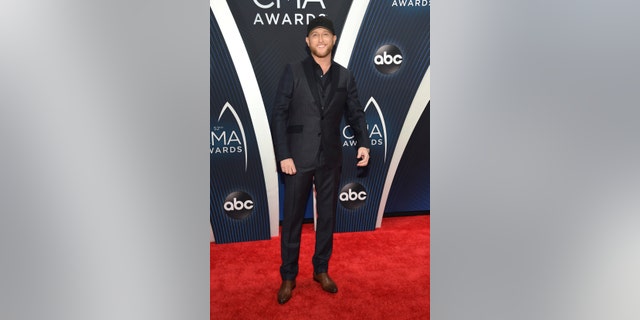 Cole Swindell wears a navy and gray suit to the CMA Awards carpet.