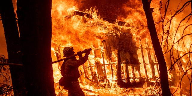 FILE - In this Nov. 9, 2018 file photo, firefighter Jose Corona sprays water as flames from the Camp Fire consume a home in Magalia, Calif. A massive new federal report warns that extreme weather disasters, like California’s wildfires and 2018’s hurricanes, are worsening in the United States. (AP Photo/Noah Berger, File)