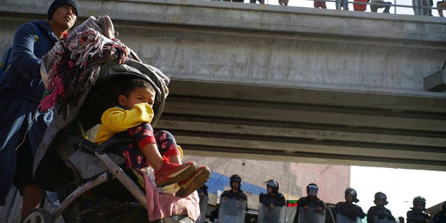 A migrant man pushes a child in a baby stroller past a cordon of riot police as he joins a small group of migrants trying to cross the border together at the Chaparral border crossing in Tijuana, Mexico, Thursday, Nov. 22, 2018. A small group of Central American migrants marched peacefully to a border crossing in Tijuana Thursday to demand better conditions and push to enter the U.S. (AP Photo/Ramon Espinosa)