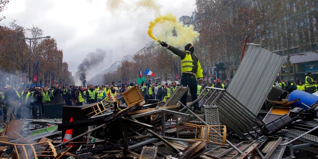 A demonstrator holds a flare on a barricade on the Champs-Elysees avenue during a demonstration against the rising of the fuel taxes, Saturday, Nov. 24, 2018 in Paris.