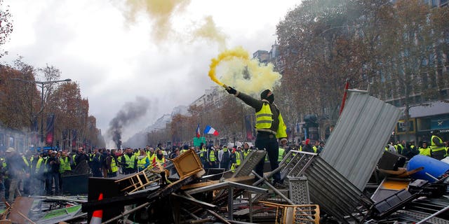 A demonstrator holds a flare on a barricade on the Champs-Elysees avenue during a demonstration against the rising of the fuel taxes, Saturday, Nov. 24, 2018 in Paris.