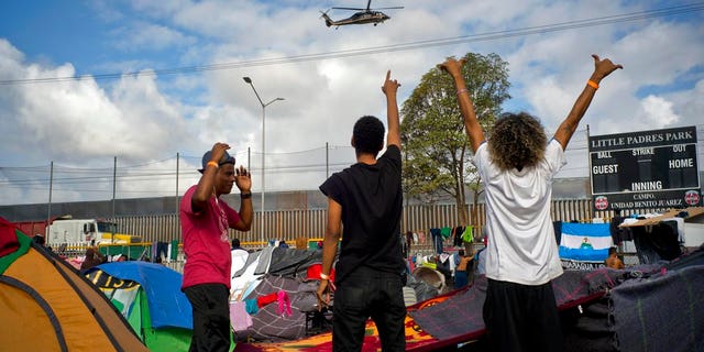 Migrants wave at U.S. border control helicopters flying near the Benito Juarez Sports Center serving as a temporary shelter for Central American migrants, in Tijuana, Mexico, Saturday, Nov. 24, 2018. The mayor of Tijuana has declared a humanitarian crisis in his border city and says that he has asked the United Nations for aid to deal with the approximately 5,000 Central American migrants who have arrived in the city. (AP Photo/Ramon Espinosa)