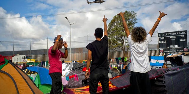 Migrants wave at U.S. border control helicopters flying near the Benito Juarez Sports Center serving as a temporary shelter for Central American migrants, in Tijuana, Mexico, Saturday, Nov. 24, 2018. The mayor of Tijuana has declared a humanitarian crisis in his border city and says that he has asked the United Nations for aid to deal with the approximately 5,000 Central American migrants who have arrived in the city. (AP Photo/Ramon Espinosa)