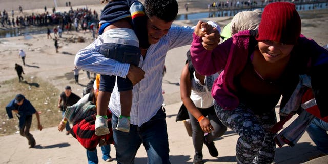 Migrants walk up a riverbank at the Mexico-U.S. border after getting past a line of Mexican police at the Chaparral border crossing in Tijuana, Mexico, Sunday, Nov. 25, 2018, as they try to reach the U.S. The mayor of Tijuana has declared a humanitarian crisis in his border city and says that he has asked the United Nations for aid to deal with the approximately 5,000 Central American migrants who have arrived in the city. (AP Photo/Ramon Espinosa)