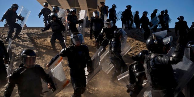 Mexican police run as they try to keep migrants from getting past the Chaparral border crossing in Tijuana, Mexico near San Ysidro, California.
