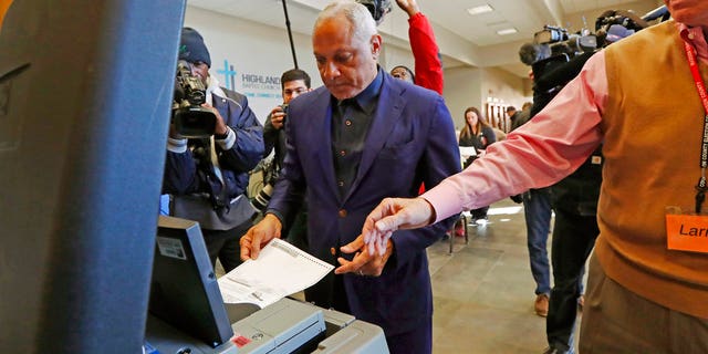 Democrat Mike Espy, left feeds his ballot into the submission machine, as directed by poll manager Larry Greer, Tuesday, Nov. 27, 2018 in Ridgeland, Miss. Mississippi voters are deciding the last U.S. Senate race of the midterms, choosing between Espy and Republican Sen. Cindy Hyde-Smith. (AP Photo/Rogelio V. Solis)