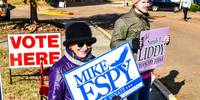 Susan Fino, left, holds a sign for U.S. Senate candidate Mike Espy and Logan Liddy holds one for Susan Liddy, a candidate for judge in the Chancery Court, District 18, Place 1 race at the Oxford Community Center in Oxford, Miss. on Tuesday, November 27, 2018. Mississippians are casting their ballots in runoff elections, including a U.S. Senate race pitting Republican Cindy Hyde-Smith against Democrat Mike Espy. (Bruce Newman/The Oxford Eagle via AP)
