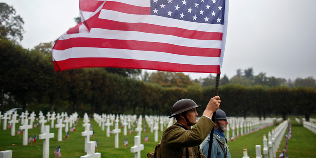 FILE In this Sunday, Sept. 23, 2018 file photo, re-enactors in World War I military uniforms carry an American flag in the Meuse-Argonne Cemetery, northeastern France. After the United States declared war on Germany in April 1917, its standing army of 127,500 became an armed force of 2 million within 1 ½ years. On Nov 11, 1918, allies like Britain and France were exhausted, Germany was as good as defeated and U.S. Gen. John J. Pershing had another 2 million troops ready to come over. (AP Photo/Thibault Camus, File)