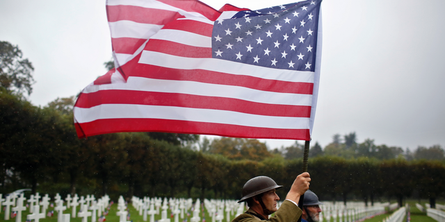 FILE In this Sunday, Sept. 23, 2018 file photo, re-enactors in World War I military uniforms carry an American flag in the Meuse-Argonne Cemetery, northeastern France. After the United States declared war on Germany in April 1917, its standing army of 127,500 became an armed force of 2 million within 1 ½ years. On Nov 11, 1918, allies like Britain and France were exhausted, Germany was as good as defeated and U.S. Gen. John J. Pershing had another 2 million troops ready to come over. (AP Photo/Thibault Camus, File)