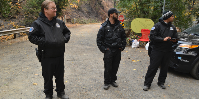 Private security guards block the road in Pulga, Calif., Monday, Nov. 12, 2018, to where investigators were trying to determine how the deadly Camp Fire started in Northern California that destroyed the town of Paradise. With the cause of the inferno under investigation, Pacific Gas & Electric Co. came under scrutiny after telling state regulators that it had been having a problem with an electrical transmission line in the area before the fire broke out. Investigators with the state fire agency were at the scene of the transmission line Monday. (AP Photo/Peter Banda)