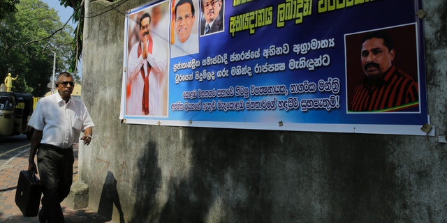 A Sri Lankan man walks past a banner carrying portraits of newly appointed prime minister Mahinda Rajapaksa, left, his brother Gotabhaya and president Maithripla Sirisena, second left, outside the supreme courts complex in Colombo, Sri Lanka, Tuesday, Nov. 13, 2018. Sri Lanka is in the midst of a political crisis set off by the president's decisions to remove the South Asian island nation's prime minister, dissolve Parliament and call snap elections. The banner reads" We welcome the leader who brought life to people" in Sinhalese. (AP Photo/Eranga Jayawardena)