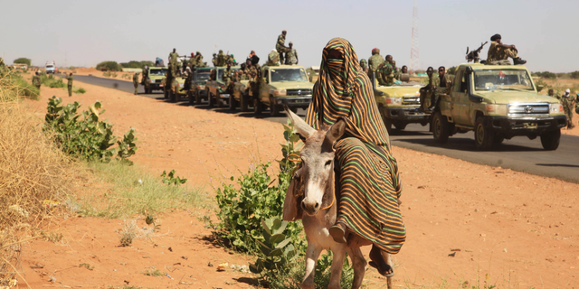 FILE - In this Thursday, Nov. 20, 2014 photo taken on a government organized media tour, a woman rides a donkey past a convoy of government troops in Tabit village in the North Darfur region of Sudan, where allegations surfaced of rape of women by government allied troops. Human Rights Watch is cautioning the United States against lifting its designation of Sudan as a state sponsor of terrorism. The New York-based watchdog said Thursday, Nov. 8, 2018 that Khartoum continues to violate basic human rights, with security forces regularly attacking civilians and opening fire on peaceful protesters.(AP Photo/Abd Raouf, File)