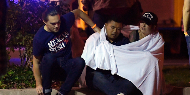 People comfort each other as they sit near the scene Thursday, Nov. 8, 2018, in Thousand Oaks, Calif. where a gunman opened fire Wednesday inside a country dance bar crowded with hundreds of people on "college night," wounding 11 people including a deputy who rushed to the scene. Ventura County sheriff's spokesman says gunman is dead inside the bar. (AP Photo/Mark J. Terrill)