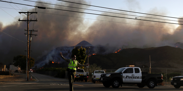 A police officer mans a checkpoint in front of an advancing wildfire Thursday, Nov. 8, 2018, near Newbury Park, Calif. The Ventura County Fire Department has also ordered evacuation of some communities in the path of the fire, which erupted a few miles from the site of Wednesday night's deadly mass shooting at a Thousand Oaks bar. (AP Photo/Marcio Jose Sanchez)