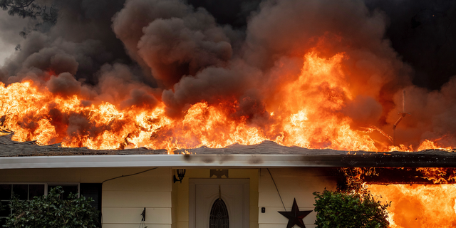 FILE- In this Thursday, Nov. 8, 2018, file photo flames consume a home as the Camp Fire tears through Paradise, Calif. Credit rating agency Moody’s on Monday estimated that insured losses for the three current fires will be between $3 billion and $6 billion. The staggering price tag is due in part to the size of the fires but also the costs of rebuilding, both materials and labor. (AP Photo/Noah Berger, File)