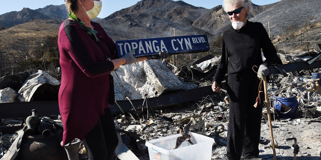 Donna Phillips, left, finds an intact street sign amid the charred possessions of her friend Marsha Maus, right, Sunday, Nov. 11, 2018, after a wildfire tore through the Seminole Springs Mobile Home Park in Agoura Hills, Calif. Maus has been a resident of the neighborhood for 15 years. (AP Photo/Chris Pizzello)