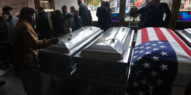 A family member places a carnation on one of the caskets of about 300 cremated remains recovered from a closed Detroit funeral home during an All Souls' Day Memorial Service, Friday, Nov. 2, 2018, at the Mount Olivet Cemetery in Detroit. Placed in five coffins, the remains will be interred at the cemetery. They were found earlier this year at Cantrell Funeral Home which was shut down in April due to improperly stored bodies and other violations. (AP Photo/Carlos Osorio)