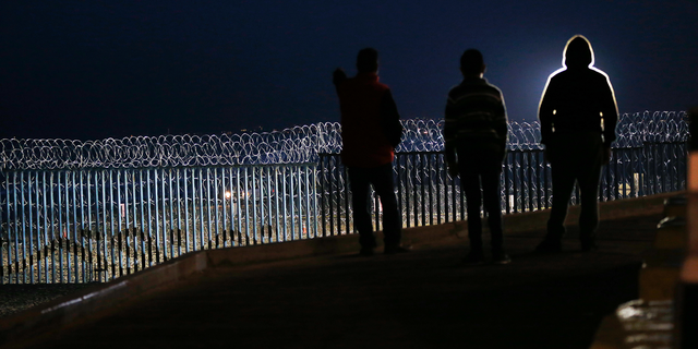Residents stand on a hill before barriers, wrapped in concertina wire, separating Mexico and the United States, where the border meets the Pacific Ocean, in Tijuana, Mexico, Saturday, Nov. 17, 2018. Many of the nearly 3,000 migrants have reached the border with California. The mayor has called the migrants' arrival an "avalanche" that the city is ill-prepared to handle. (AP Photo/Marco Ugarte)