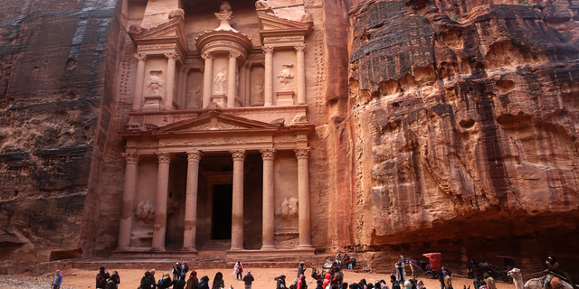FILE - In this Feb. 13, 2017, file photo, tourists brave a rare rainstorm in plastic ponchos to peer at the Treasury, Jordan's most famous archaeological monument leftover from the Nabatean civilization in the kingdom's Petra archaeological park. Flash floods caused by heavy rain across Jordan killed people Friday, Nov. 9, 2018 and forced hundreds of tourists to seek higher ground in the kingdom's ancient city of Petra, the government spokeswoman said. (AP Photo/Sam McNeil, File)