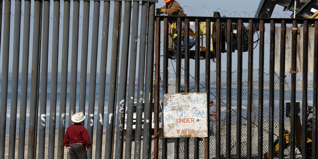 A man on the U.S. side of the border, top, works on the border structure as a man standing on the beach looks on, seen from Tijuana, Mexico, Thursday, Nov. 15, 2018. Members of a migrant caravan from Central America continued to arrive by the hundreds in the Mexican border city of Tijuana. (AP Photo/Gregory Bull)