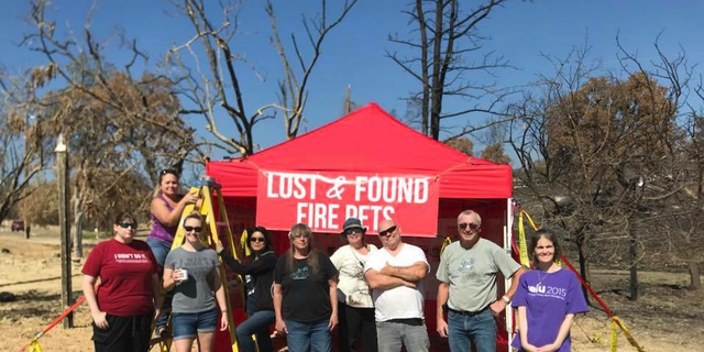 In this undated photo, Volunteers with Carr Fire Pet Rescue and Reunification pose with their "Lost and Found Fire Pets" kiosk in Redding, Calif. Volunteers continue to track and catch missing pets nearly two months after the fire was extinguished. They post pictures of the rescued pets in hopes that their owners will recognize them and reunite with them. More than 80 families who lost their homes in California's deadly Carr Fire in July have learned weeks or months later that their dogs and cats had survived the deadly disaster. (Courtesy of Stacey Jimenez via AP)