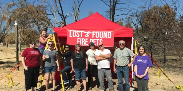 In this undated photo, Volunteers with Carr Fire Pet Rescue and Reunification pose with their "Lost and Found Fire Pets" kiosk in Redding, Calif. Volunteers continue to track and catch missing pets nearly two months after the fire was extinguished. They post pictures of the rescued pets in hopes that their owners will recognize them and reunite with them. More than 80 families who lost their homes in California's deadly Carr Fire in July have learned weeks or months later that their dogs and cats had survived the deadly disaster. (Courtesy of Stacey Jimenez via AP)