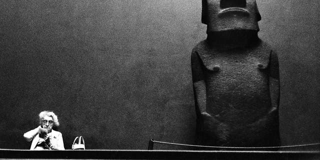 An elderly woman sits reading by a large stone statue, or moai from Easter Island on display at the British Museum, London, 1967. (Photo by Romano Cagnoni/Hulton Archive/Getty Images)