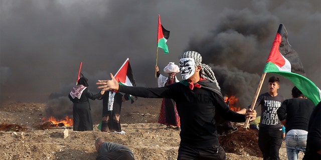 Protesters wave their national flags while others burn tires near the fence of Gaza Strip border with Israel during a protest east of Gaza City, Friday, Nov. 9. Gaza's Hamas rulers said Friday that deadly protests along Gaza-Israel perimeter fence have achieved some goals; $15 million from Qatar to help pay the salaries of civil servants. (AP Photo/Adel Hana)