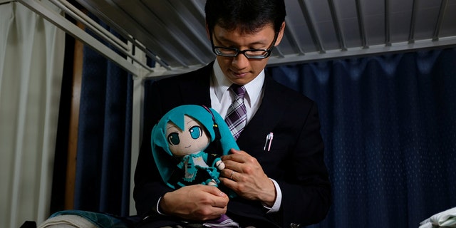 Akihiko Kondo, 35, poses for a photograph with a doll modeled after virtual reality singer Hatsune Miku, wearing their wedding rings, at his apartment after marrying her in Tokyo, Japan.