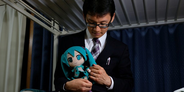 Akihiko Kondo, 35, poses for a photograph with a doll modeled after virtual reality singer Hatsune Miku, wearing their wedding rings, at his apartment after marrying her in Tokyo, Japan.
