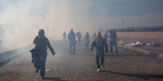 Migrants run from tear gas launched by U.S. agents, amid photojournalists covering the Mexico-U.S. border, after a group of migrants got past Mexican police at the Chaparral crossing in Tijuana, Mexico, Sunday, Nov. 25, 2018. The mayor of Tijuana has declared a humanitarian crisis in his border city and says that he has asked the United Nations for aid to deal with the approximately 5,000 Central American migrants who have arrived in the city. (AP Photo/Rodrigo Abd)