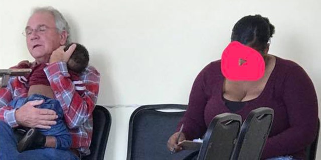 Joe Hale holds Jade West's son Jayce as she fills out paperwork at the doctor's office. A post on social media about the two strangers went viral commenting on the "hope" this moment gave.