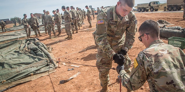 U.S. Army soldiers, assigned to 309th Military Intelligence Battalion and 305th Military Intelligence Battalion, working together to hammer a stake into the ground while setting up tents on Fort Huachuca, Arizona, on Thursday.