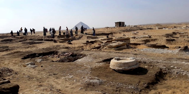 This undated photo released by the Egyptian Ministry of Antiquities on Wednesday, Nov. 28, 2018, shows archaeologists standing near an ancient mummy which was found inside a sarcophagus in an area of King Amenemhat II's pyramid in the Dahshur royal necropolis. (Egyptian Ministry of Antiquities via AP)