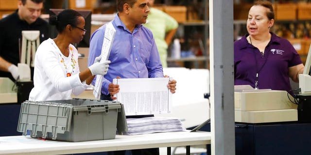 Employees at the Palm Beach County Supervisor of Elections office feed ballots through a machine as they count votes during a recount, Tuesday, Nov. 13, 2018, in West Palm Beach, Fla. (AP Photo/Wilfredo Lee)